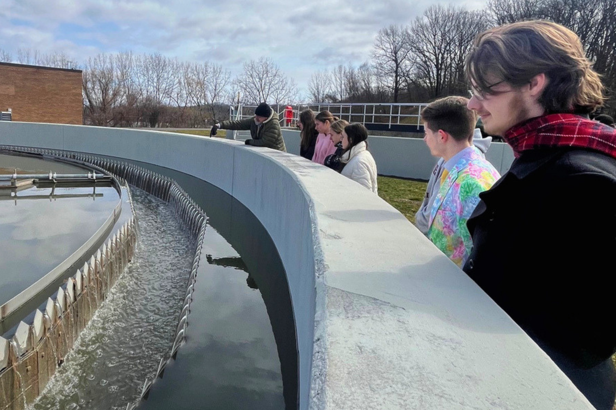Students stand around a water reservoir while a man points into the water